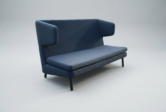 Bolia loungesofa i blå polstring med højt ryglæn, afrundede armlæn og slanke sorte ben set skråt.