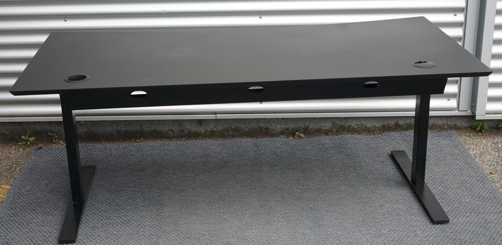 Dencon hæve-sænkebord 160x90 i sort linoleum set bagfra med kabelbakker og robust understel.