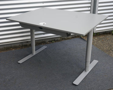 Denconi hæve-sænkebord 120x80 cm i lysegrå laminat med robust T-stel, set fra skrå vinkel.