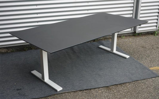 Holmris hæve-sænkebord 200x100 med sort linoleum bordplade og affasede kanter, set fra skrå vinkel med kabelbakke.