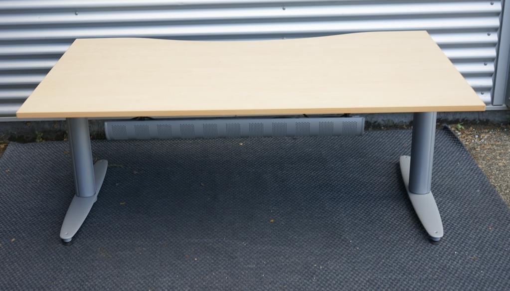 Bagfra visning af Kinnarps hæve-sænkebord i ahornfiner med gråt stel og integreret kabelbakke.