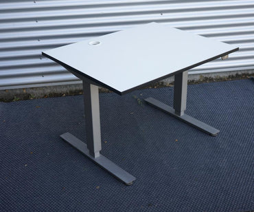 Kinnarps hæve-sænkebord i hvid set i skrå vinkel. Elektrisk hæve-sænkebord med kompakt bordplade 100x80 cm, perfekt til små arbejdspladser.