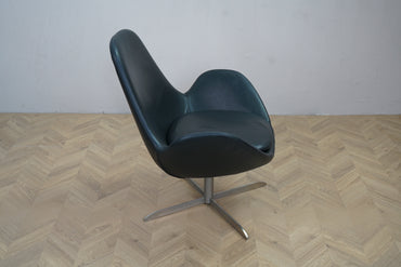 Elegant lænestol i sort læder med brede armlæn og metal-drejefod set fra siden