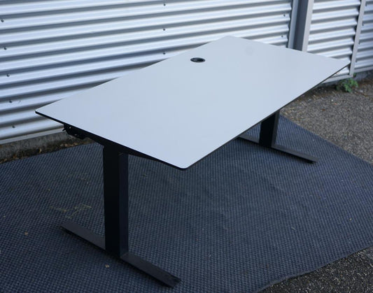 Martela hæve-sænkebord 160x80 cm med hvid bordplade, sort stel og affasede kanter, set fra skrå vinkel med integreret stikdåse og kabelbakke.