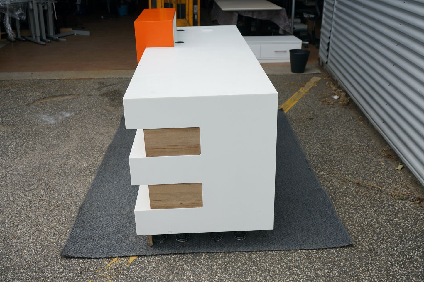 Receptionsbord set fra siden – minimalistisk design i hvid og træ med orange front.