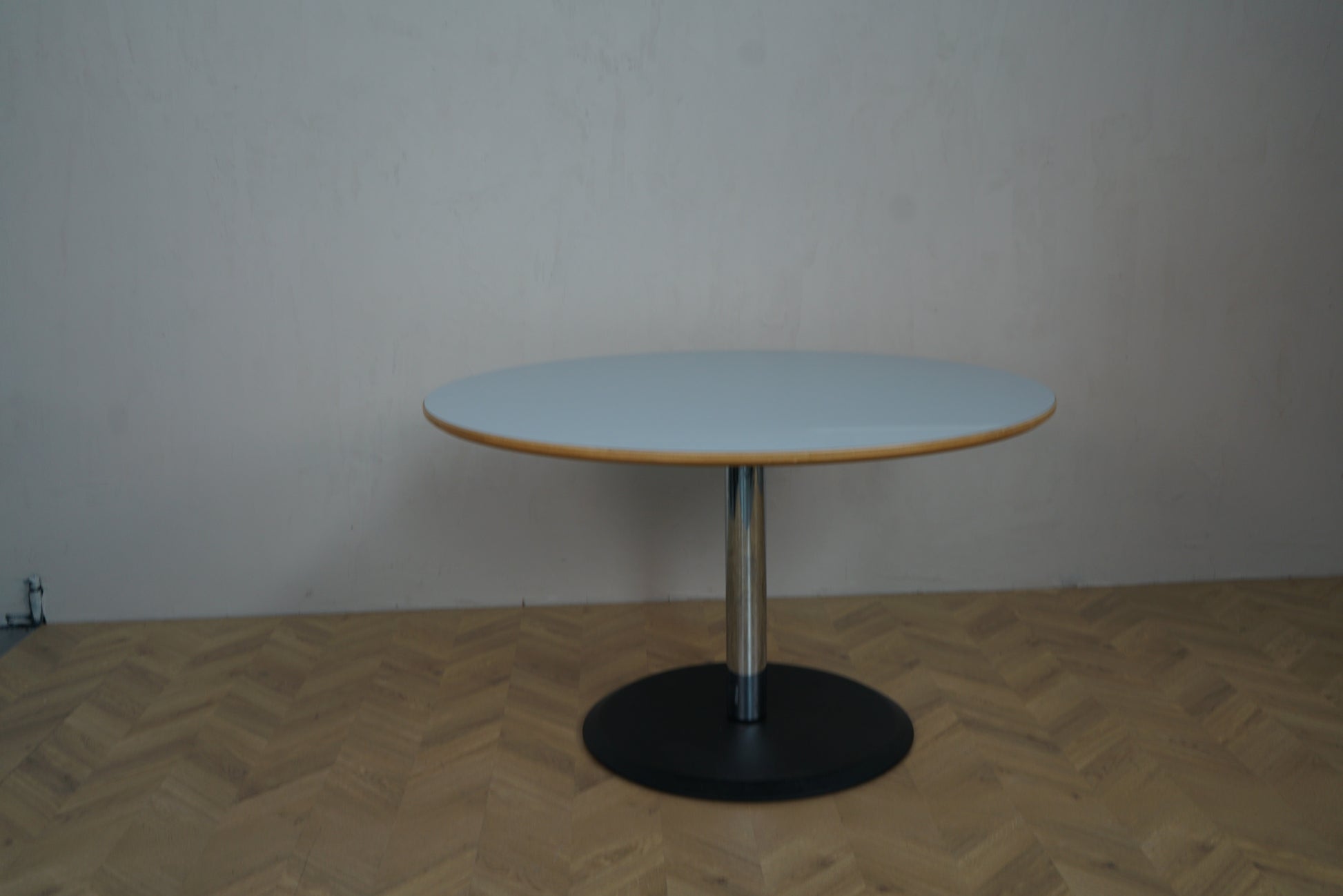 Stilrent rundt bord Ø124 cm med lyseblå bordplade og sort fod set på afstand – mødebord, cafébord eller spisebord