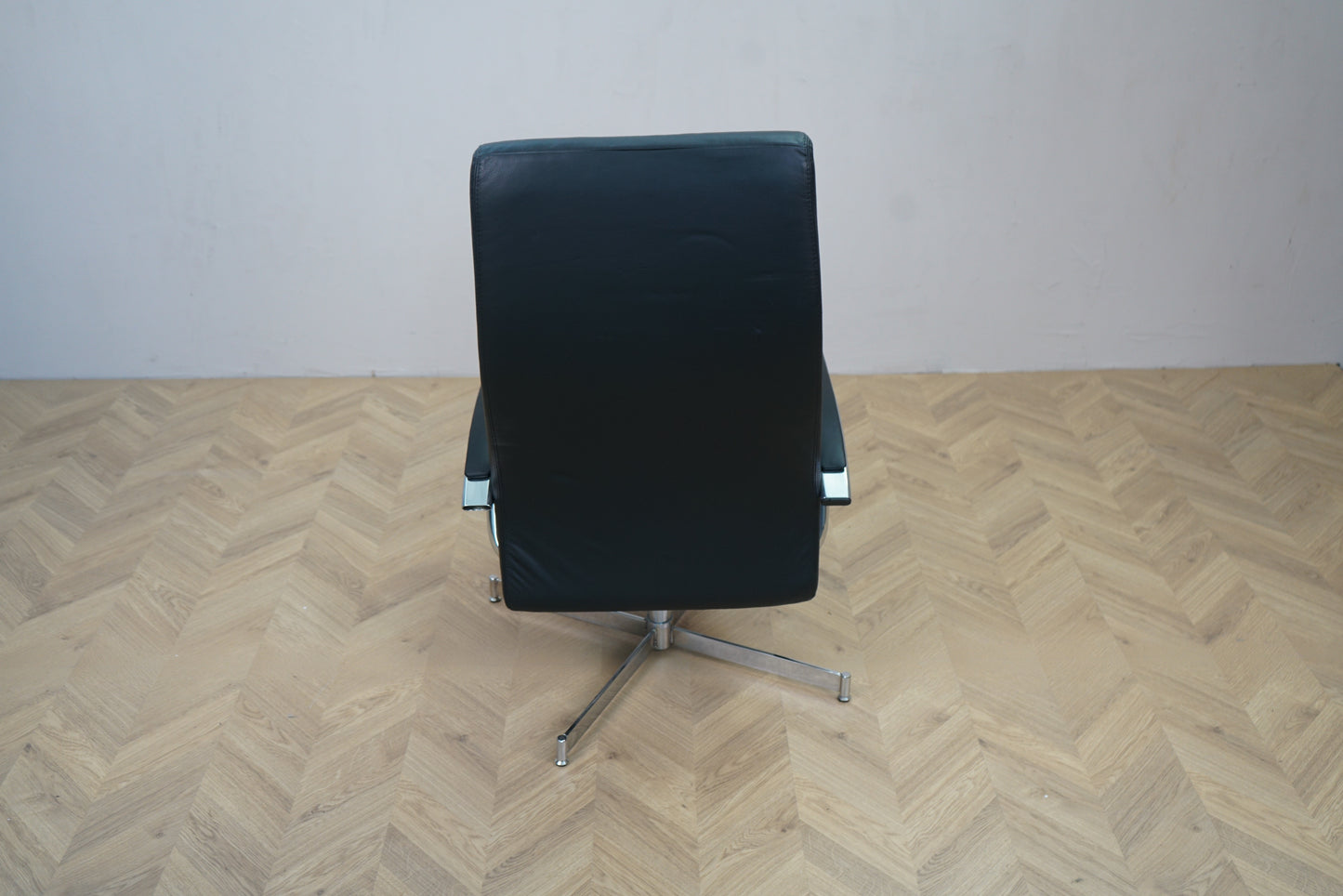 Loungestol i sort læder med slankt design og solid drejefod set bagfra