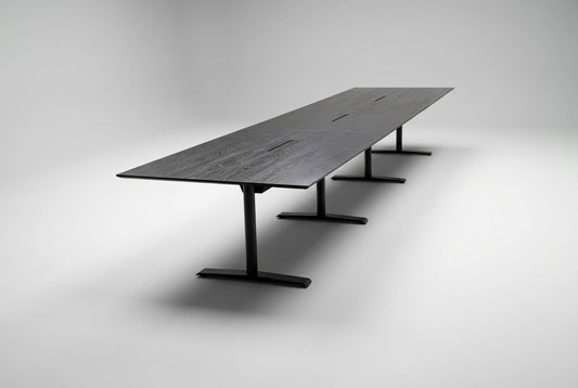 Stort konferencebord i sort eg med sort stel, affaset kant og kabelgennemføringer, 500x120 cm, set fra skrå vinkel.