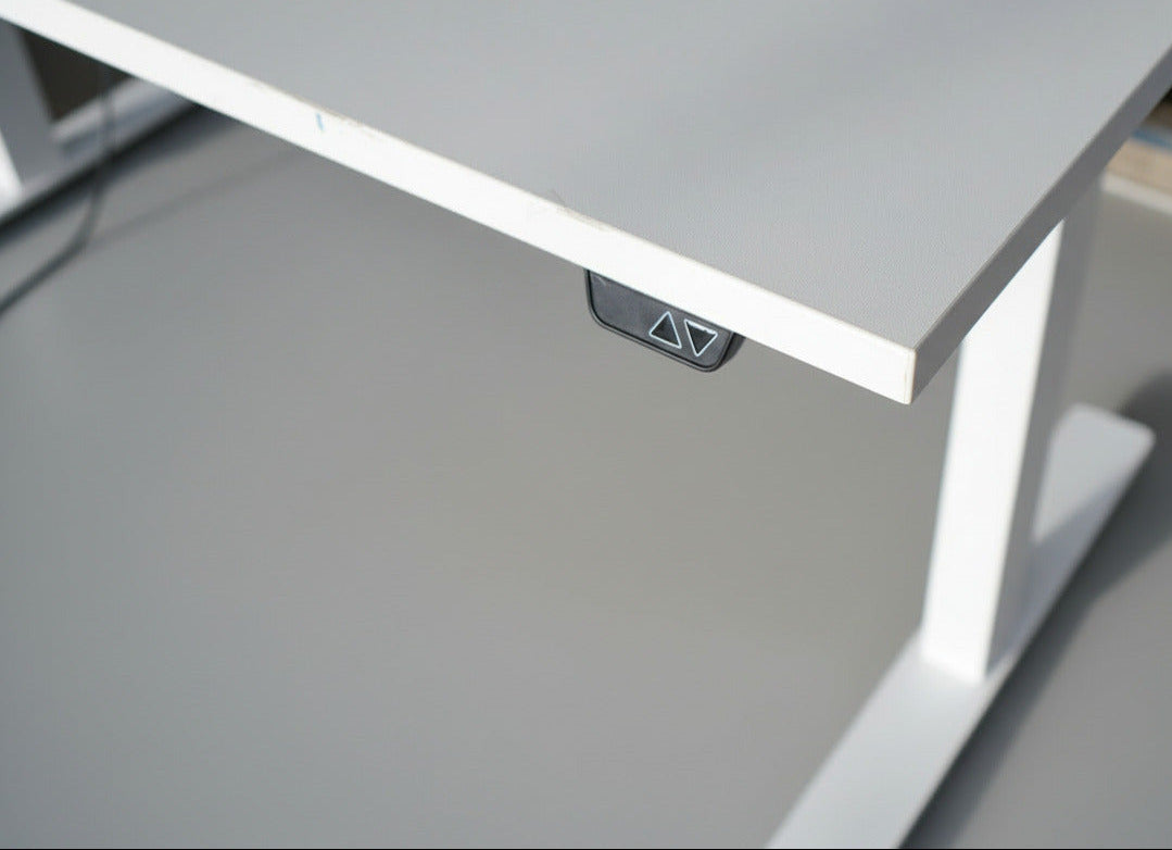 Close-up af hvid laminatbordplade og detaljer på AJ Products hæve-sænkebord med kabelbakke.