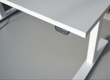 Close-up af hvid laminatbordplade og detaljer på AJ Products hæve-sænkebord med kabelbakke.