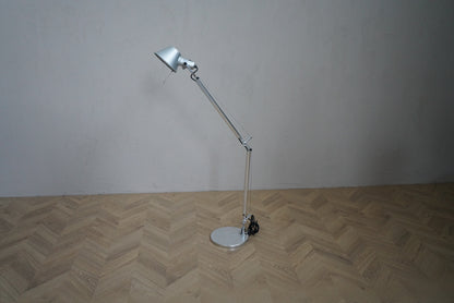 Artemide Tolomeo bordlampe i aluminium med rund fod, justerbar arm og bevægeligt lampehoved, set forfra.