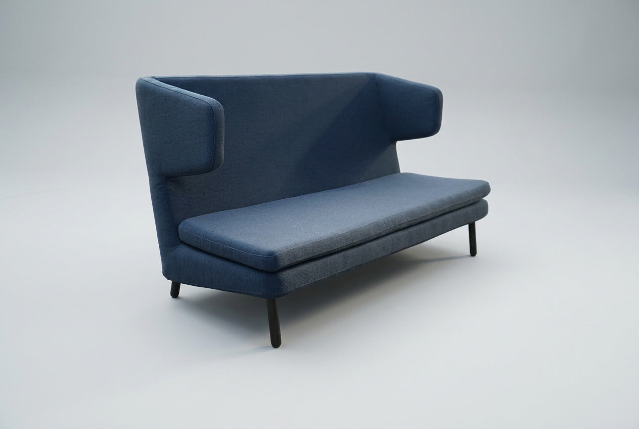 Bolia loungesofa i blå polstring med højt ryglæn, afrundede armlæn og slanke sorte ben set skråt.