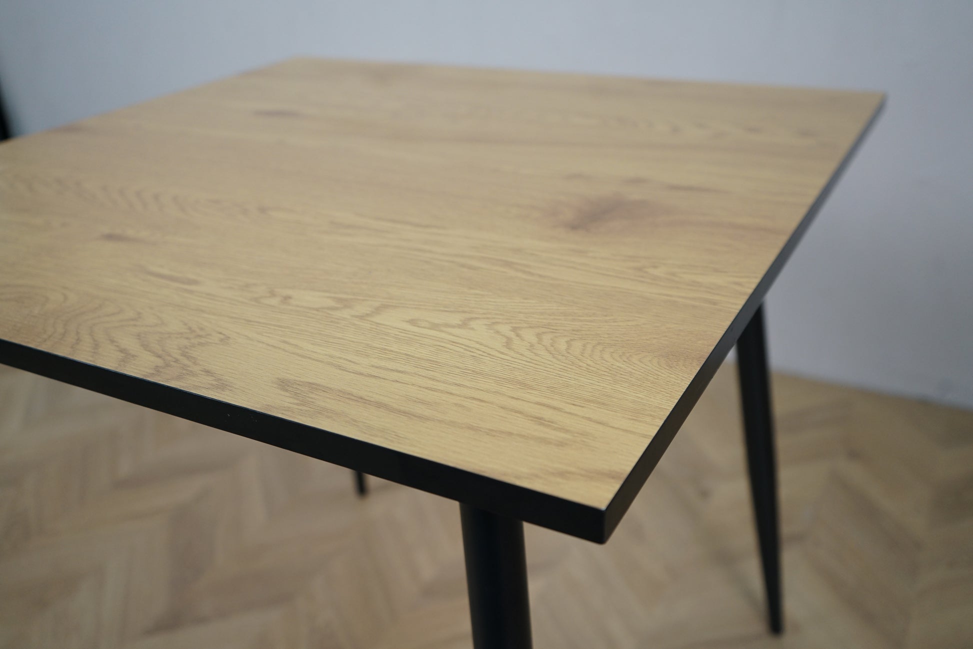 Detalje af Carnett spisebord – nærbillede af lakeret bordplade i grå trælook og pulverlakeret sort understel.