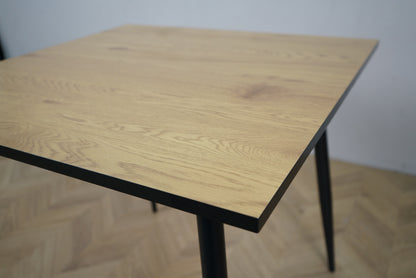 Detalje af Carnett spisebord – nærbillede af lakeret bordplade i grå trælook og pulverlakeret sort understel.