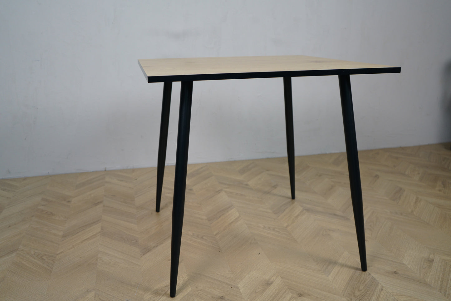 Carnett spisebord set fra lige vinkel – rektangulært bord i grå trælook med sort stel, perfekt til café eller spiseområde.