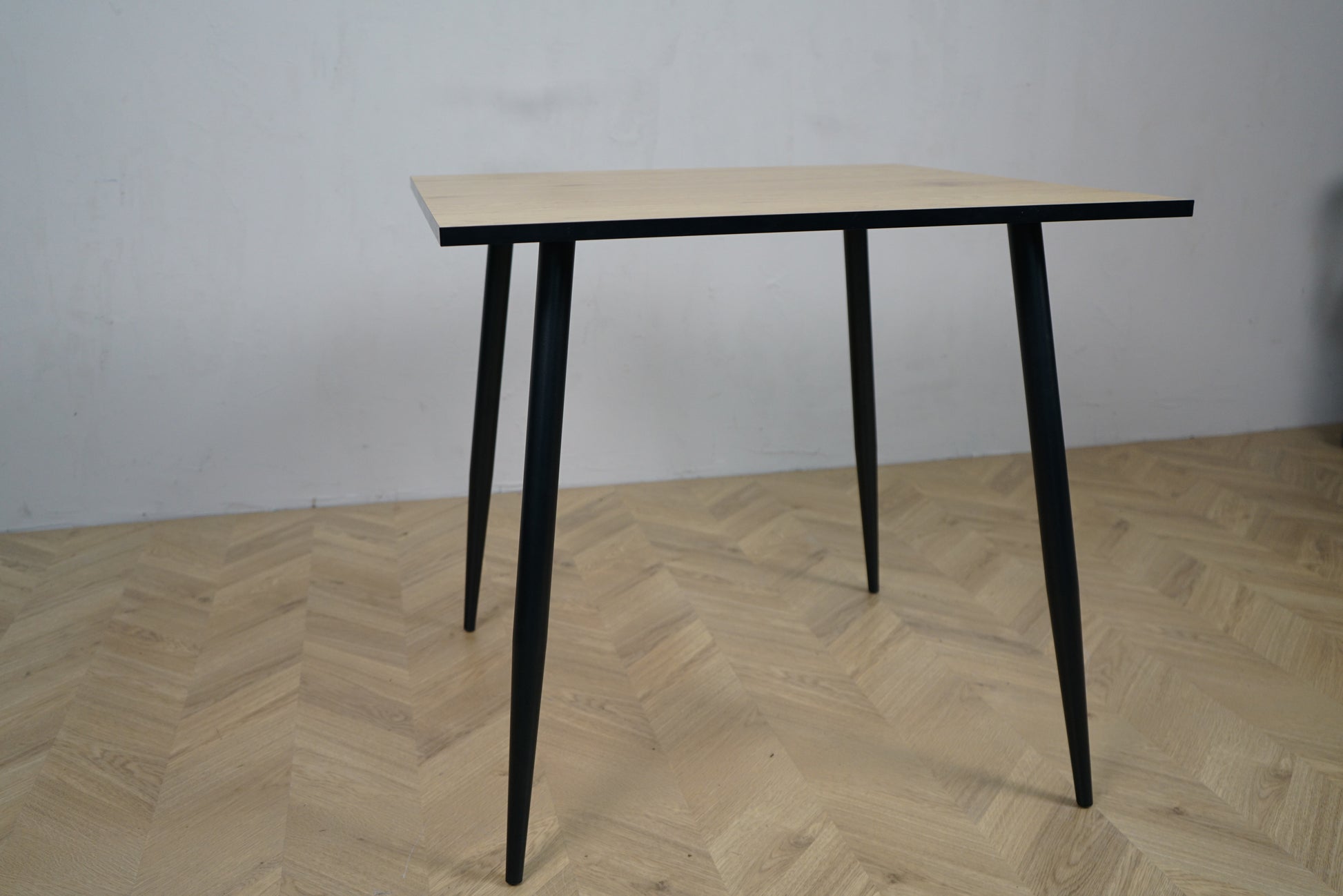 Carnett spisebord set fra lige vinkel – rektangulært bord i grå trælook med sort stel, perfekt til café eller spiseområde.