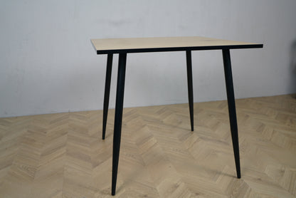 Carnett spisebord set fra lige vinkel – rektangulært bord i grå trælook med sort stel, perfekt til café eller spiseområde.