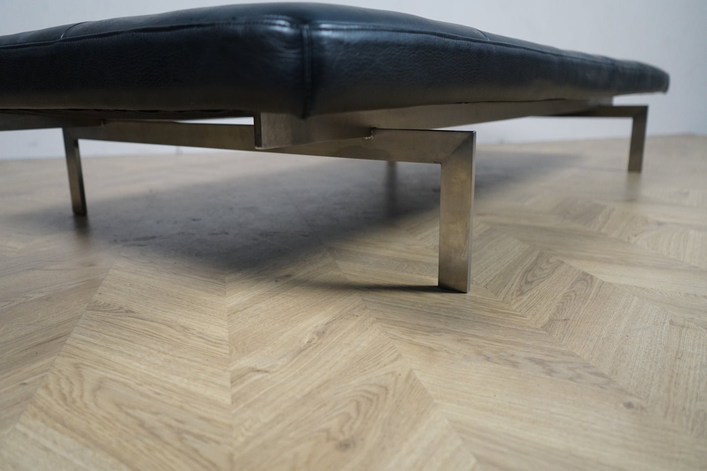 dagseng fotograferet nedefra med fokus på forkromede stålben og sort læderpolstring.