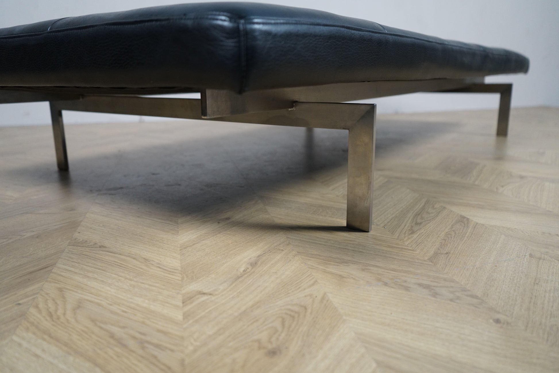 dagseng fotograferet nedefra med fokus på forkromede stålben og sort læderpolstring.