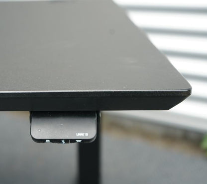 Close-up af Dencon hæve-sænkebord 130x80 med detaljer af sort linoleum bordplade og affasede kanter.