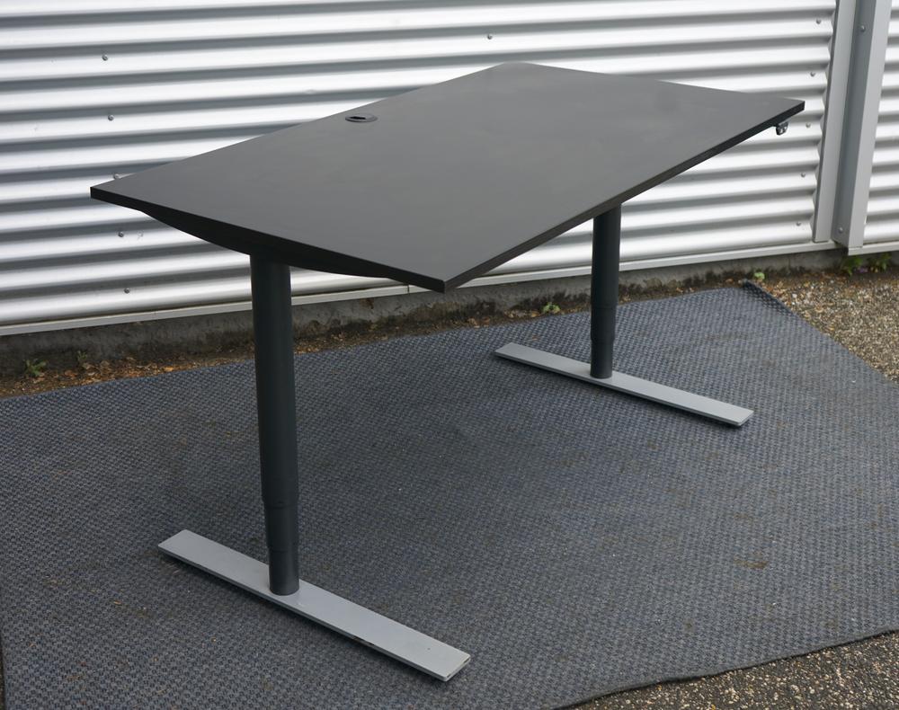 Dencon hæve-sænkebord 140x80 cm i sort med justerbar højde og kabelgennemføring, set fra skrå vinkel.