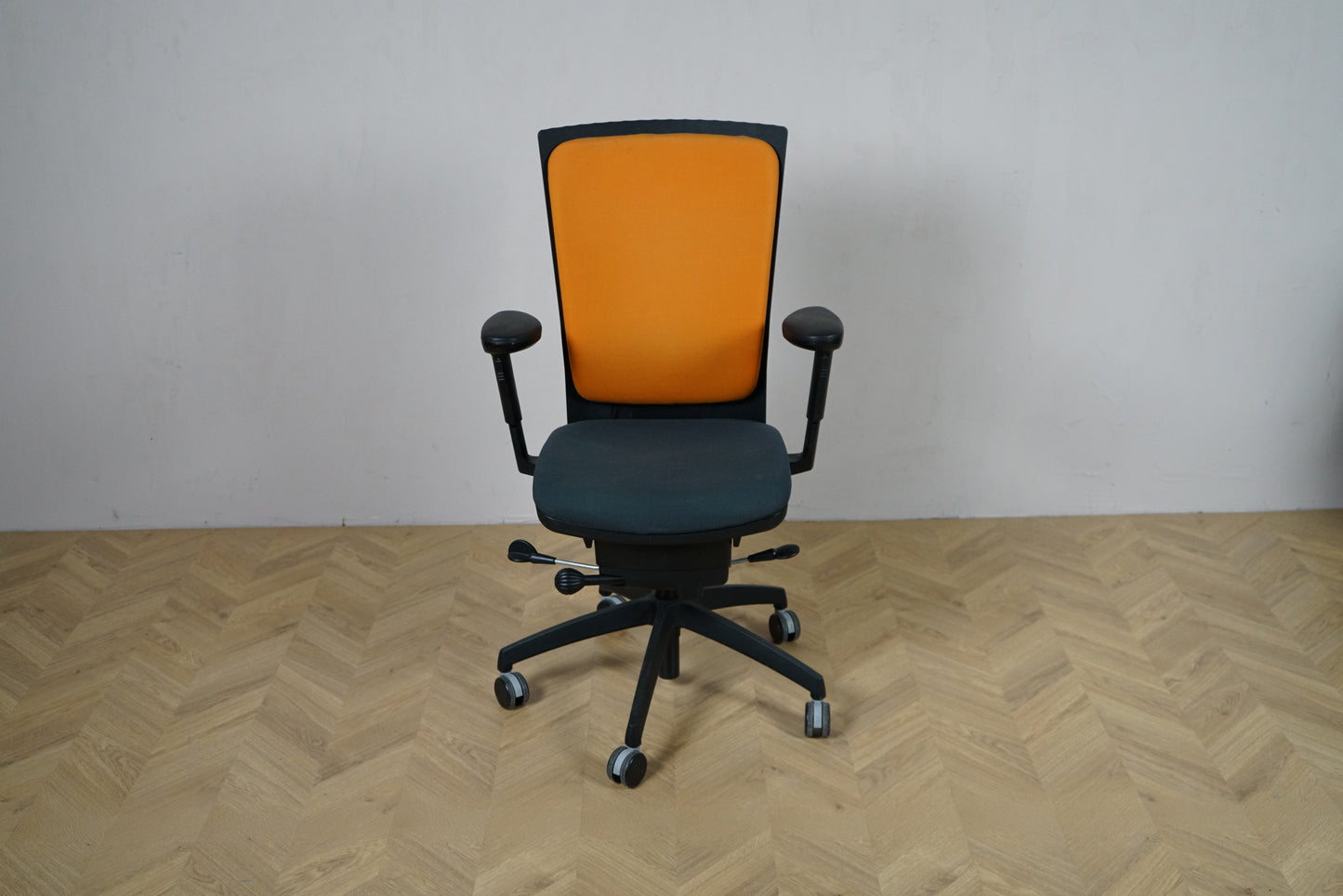 EFG kontorstol set forfra med orange polstret ryglæn, mørkt sæde og armlæn samt sort fodkryds.