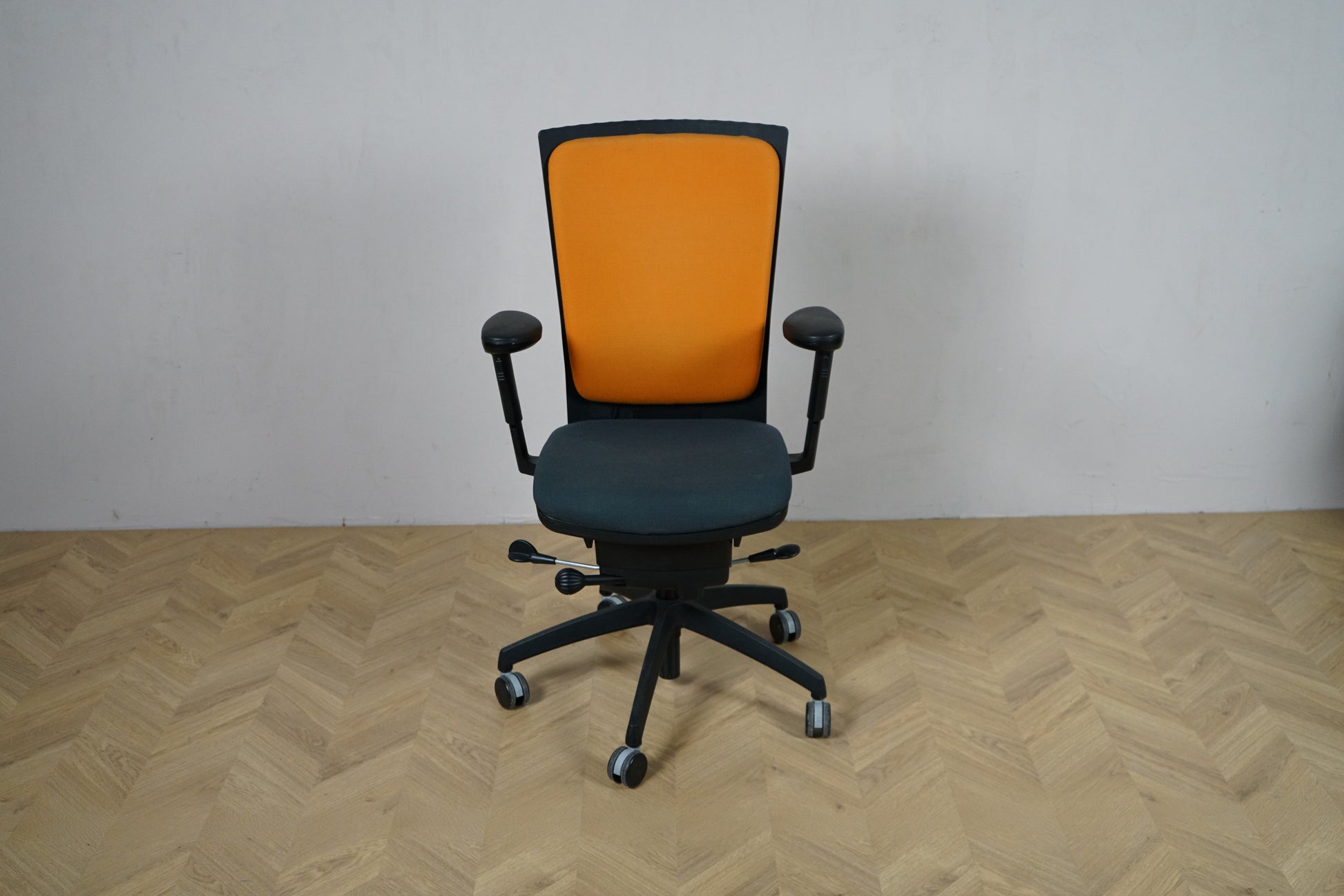 EFG kontorstol set forfra med orange polstret ryglæn, mørkt sæde og armlæn samt sort fodkryds.