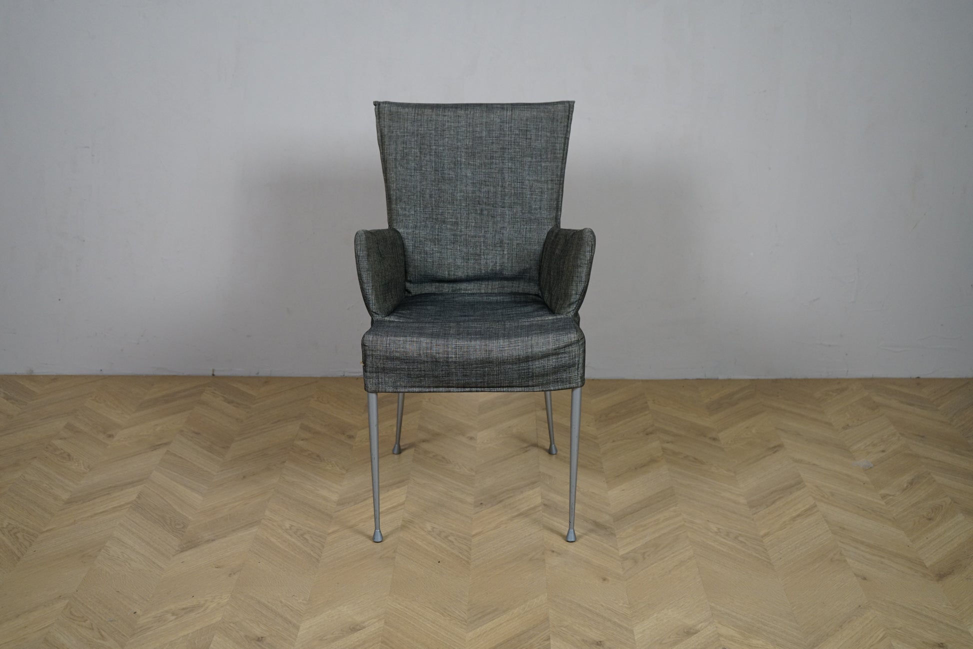 Grå polstret loungestol med armlæn og metalstel set forfra