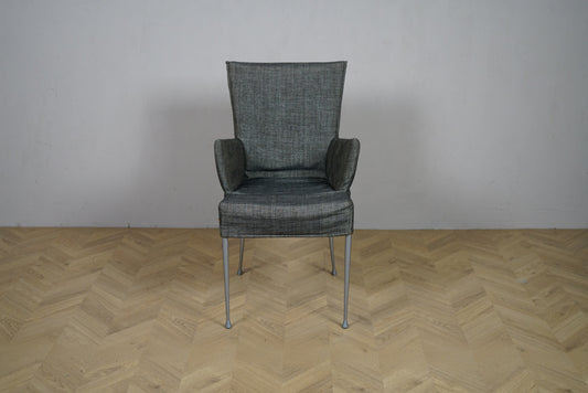 Grå polstret loungestol med armlæn og metalstel set forfra