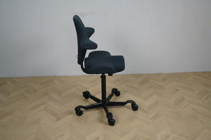 HÅG Capisco 8106 set fra siden med ergonomisk sadelsæde, justerbart ryglæn, sort aluminiumsfodkryds og gummibanehjul.