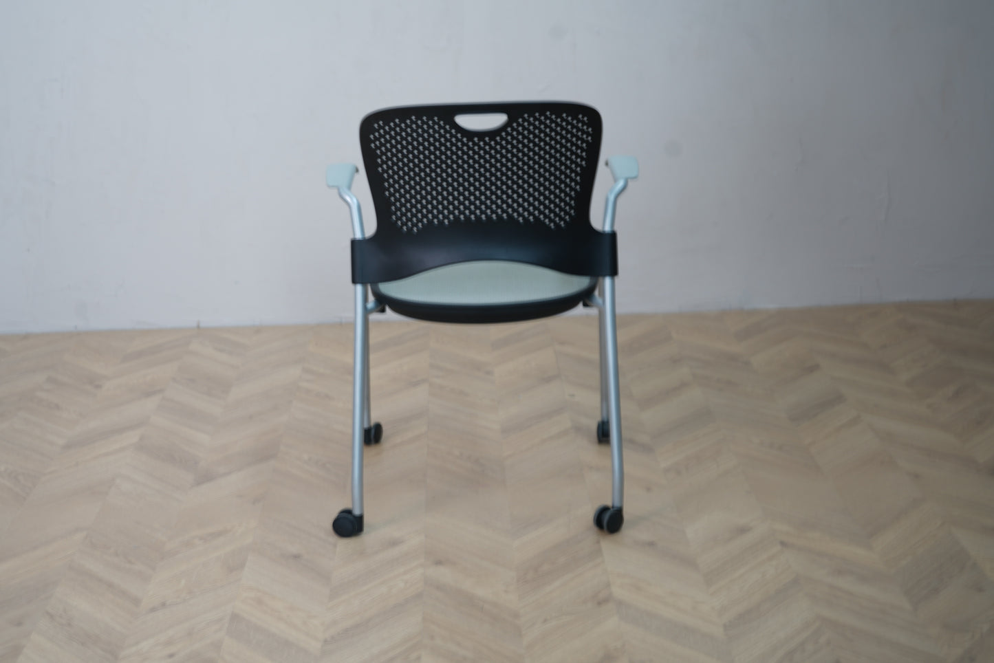 Herman Miller Casper konferencestol med hjul set bagfra, perforeret sort ryglæn og grålakeret metalstel.