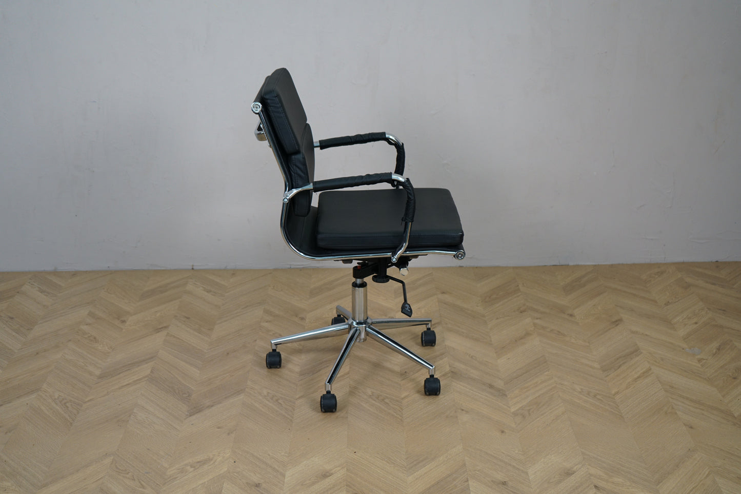 Konferencestol i sort læder set fra siden med lav ryg og armlæn