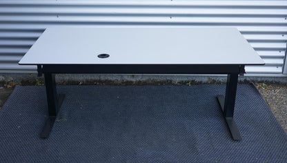 Bagfra visning af Martela hæve-sænkebord 160x80 cm med sort stel, kabelbakke og integreret strømudtag under bordpladen.