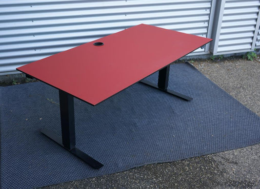 Martela hæve-sænkebord i rød linoleum 160x80 cm set fra skrå vinkel – ergonomisk skrivebord med affasede kanter og kabelbakke.