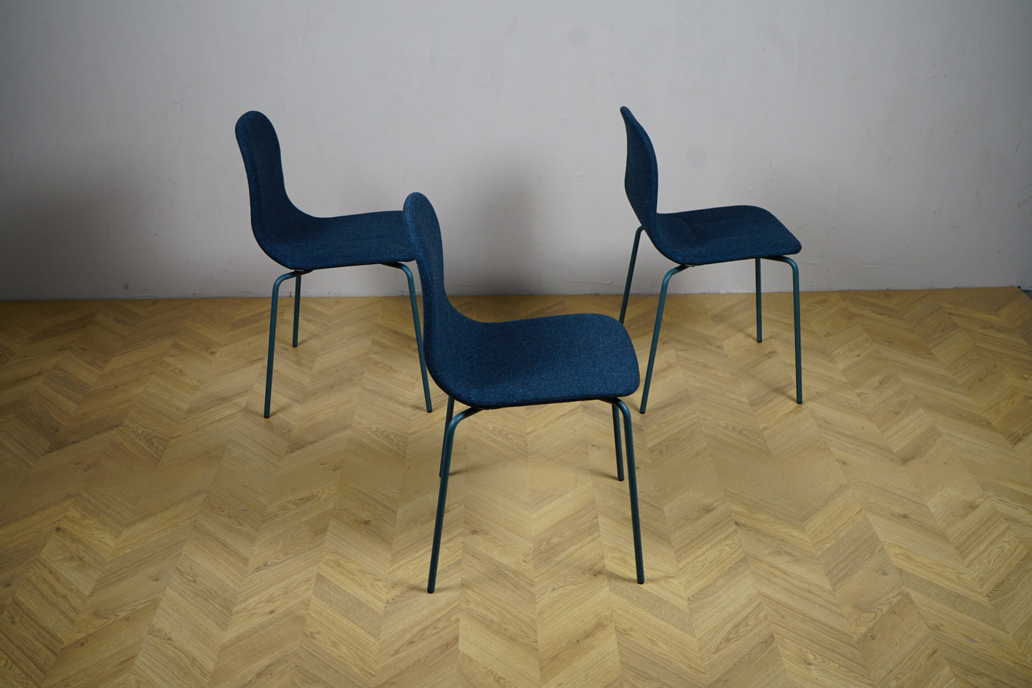 Sidevinkel af 3 Materia stabelbare stole i mørkeblå polstret uldstof – minimalistisk og ergonomisk design.