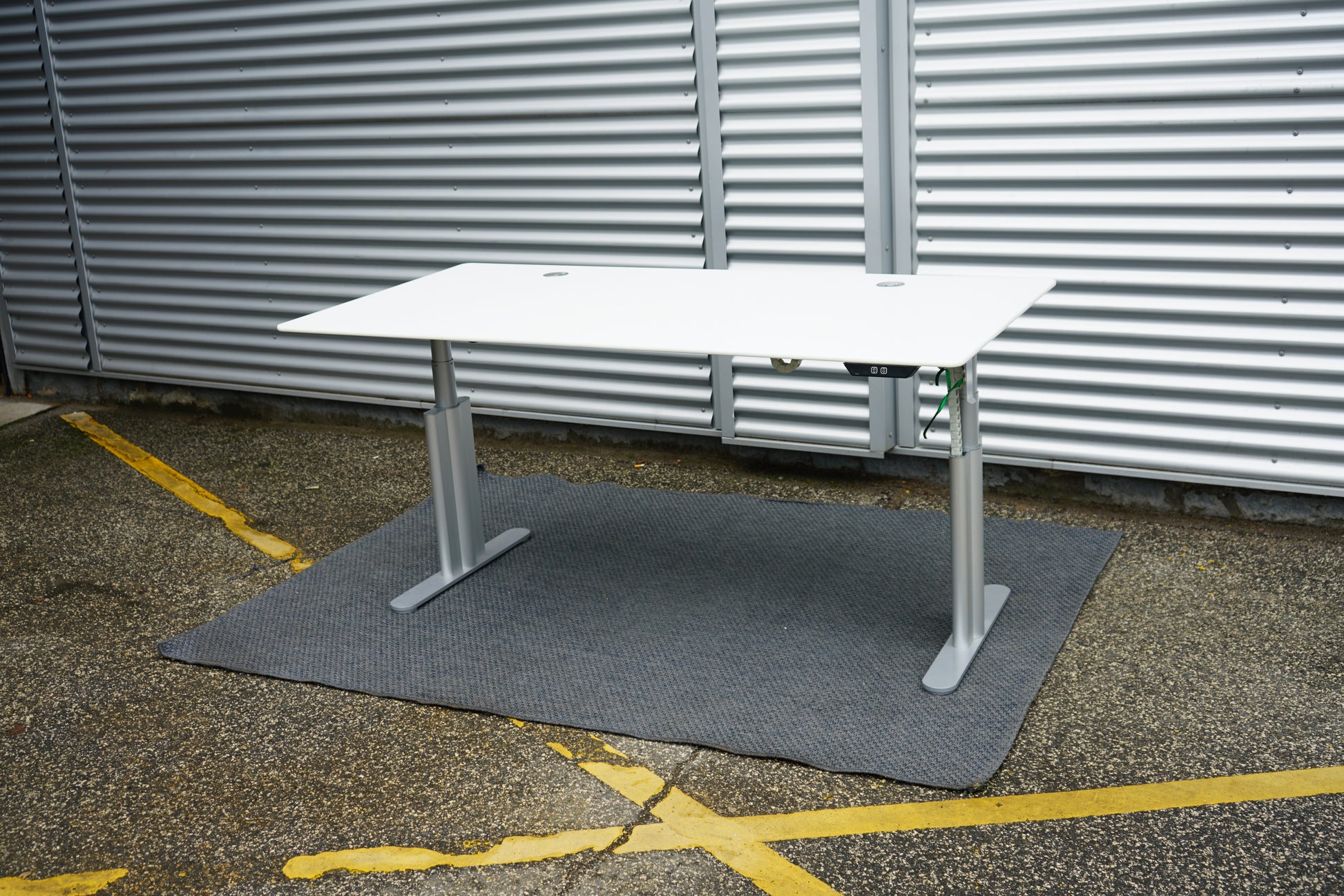 Montana hæve-sænkebord fotograferet fra skrå vinkel med hvid bordplade og sølv stel, 180x90 cm med kabelgennemføringer.