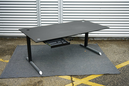 Rumas hæve-sænkebord i sort linoleum 180x90 cm med skuffe og stikkontakt set fra skrå vinkel