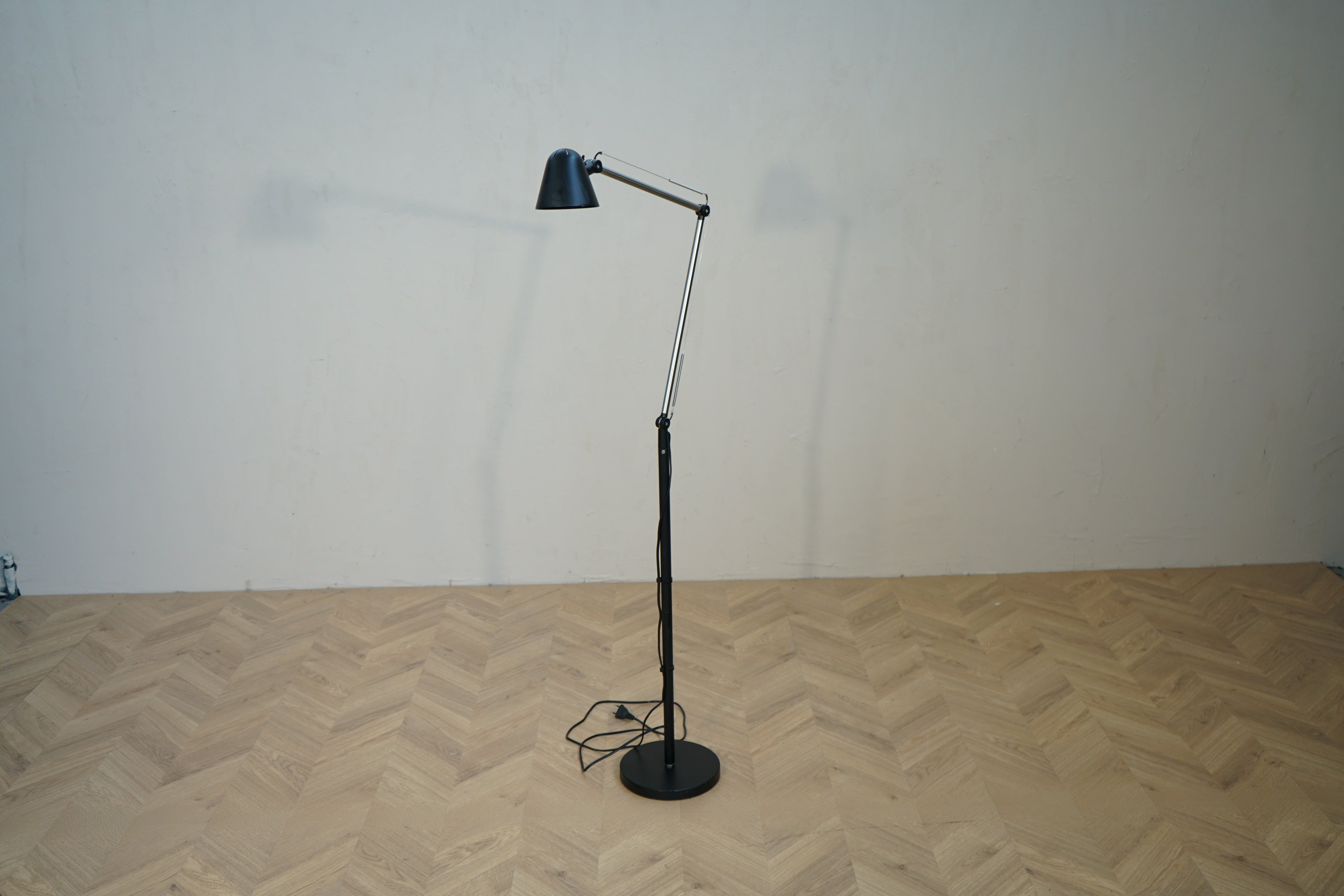 Sort gulvlampe med justerbar arm og lampeskærm set forfra.