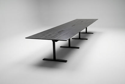 Stort konferencebord i sort eg med sort stel, affaset kant og kabelgennemføringer, 500x120 cm, set fra skrå vinkel.