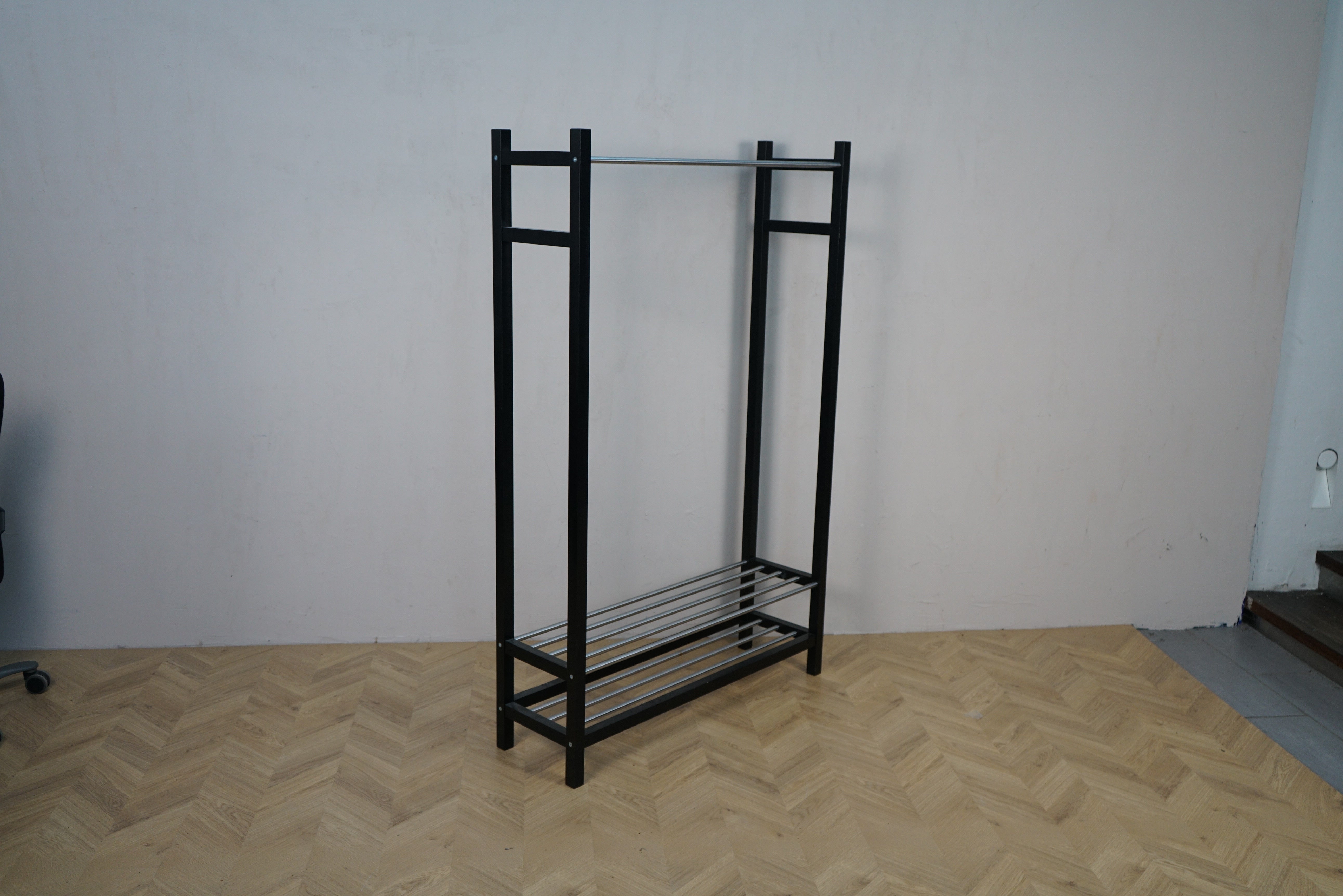 Sort tøjstativ i metal med hylde og bøjlestang set i skrå vinkel